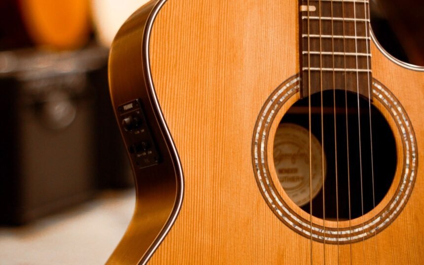 Solid spruce-top compact acoustic guitar with a side-mounted piezo pickup preamp, other guitars visible in a shop rack behind it