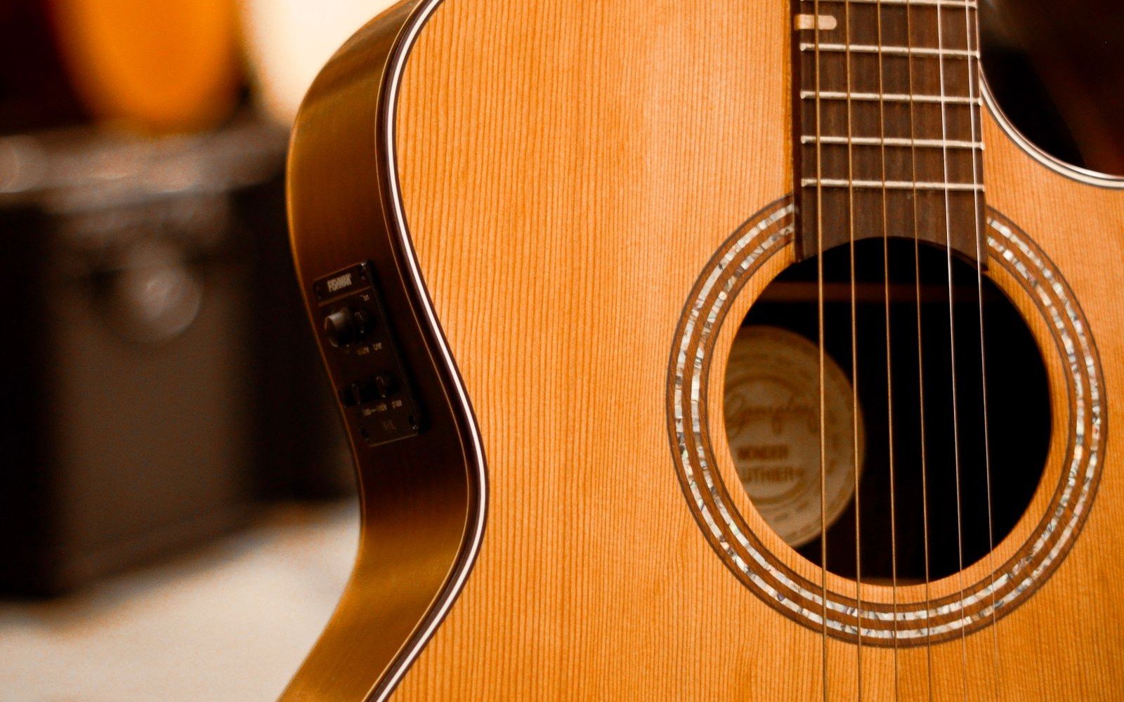 Solid spruce-top compact acoustic guitar with a side-mounted piezo pickup preamp, other guitars visible in a shop rack behind it