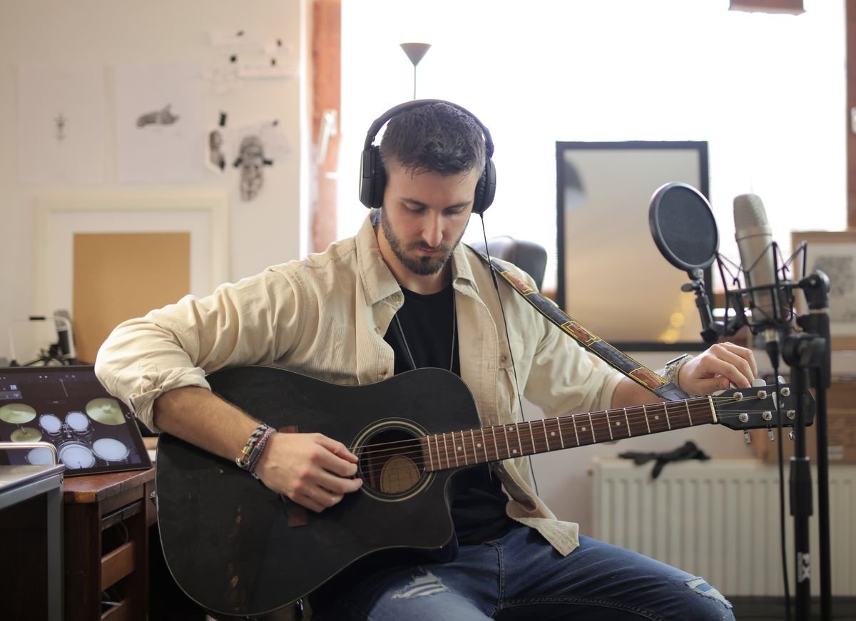Guitarist adjusting an acoustic guitar while wearing headphones in a home studio