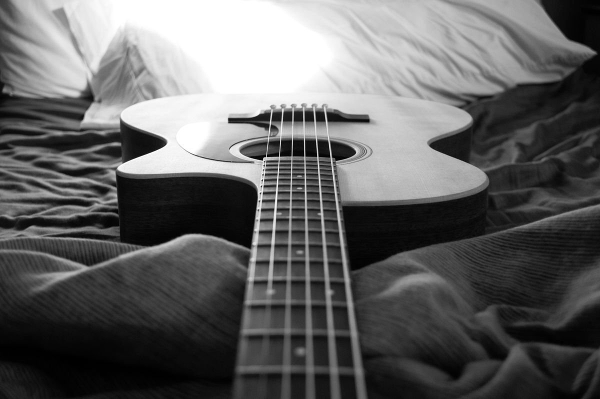 A full-size acoustic guitar resting on a bed, illustrating the size and space a standard guitar takes up at home