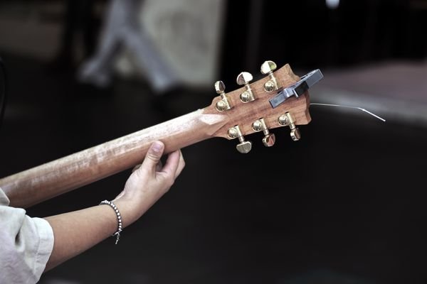 A hand tuning the gold machine heads on a wood-bodied travel acoustic guitar headstock