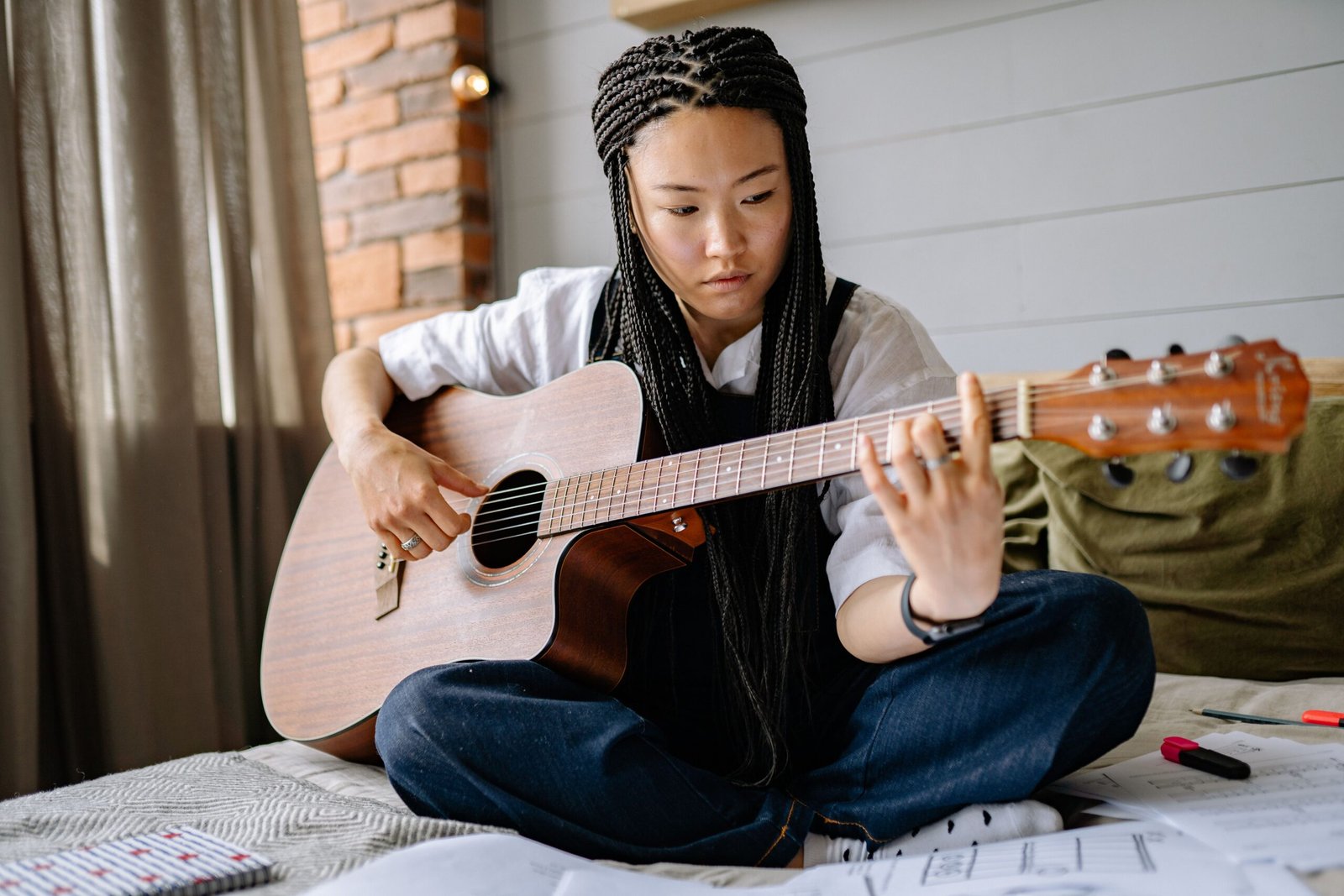 A woman sitting cross-legged on a bed playing an acoustic guitar