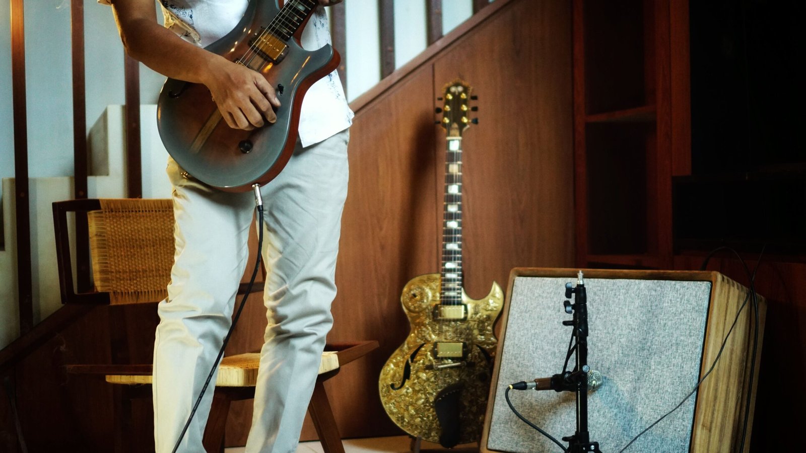 A man playing an electric guitar plugged in next to an amplifier and a microphone stand