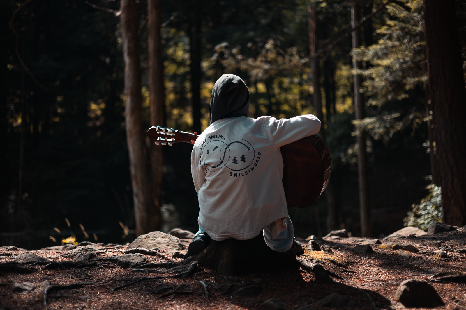 A guitarist sitting on a log playing an acoustic guitar in a forest, the kind of setting a travel guitar for camping needs to handle