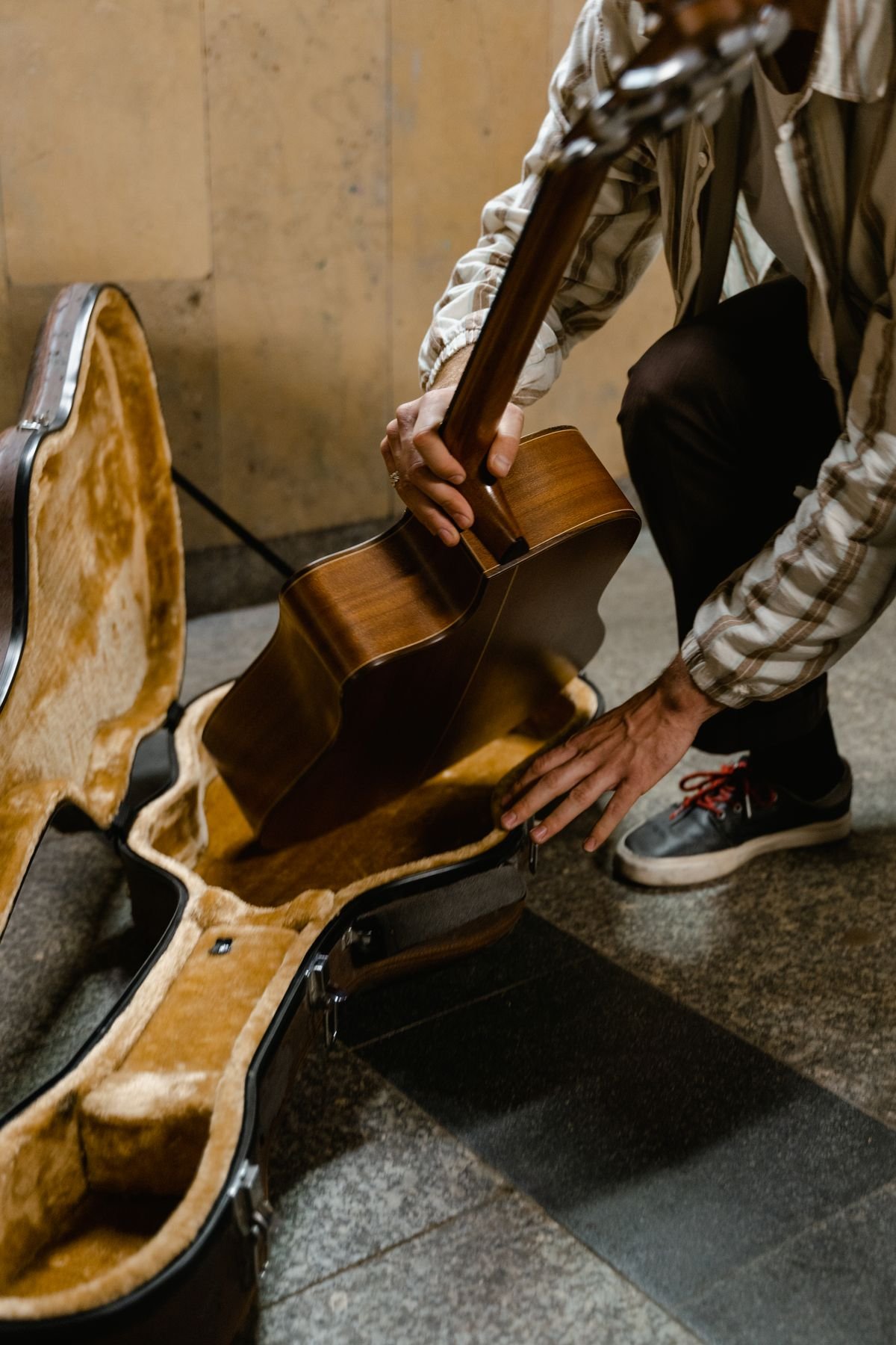 A guitarist lowering an acoustic guitar into a padded hardshell case, ready to travel