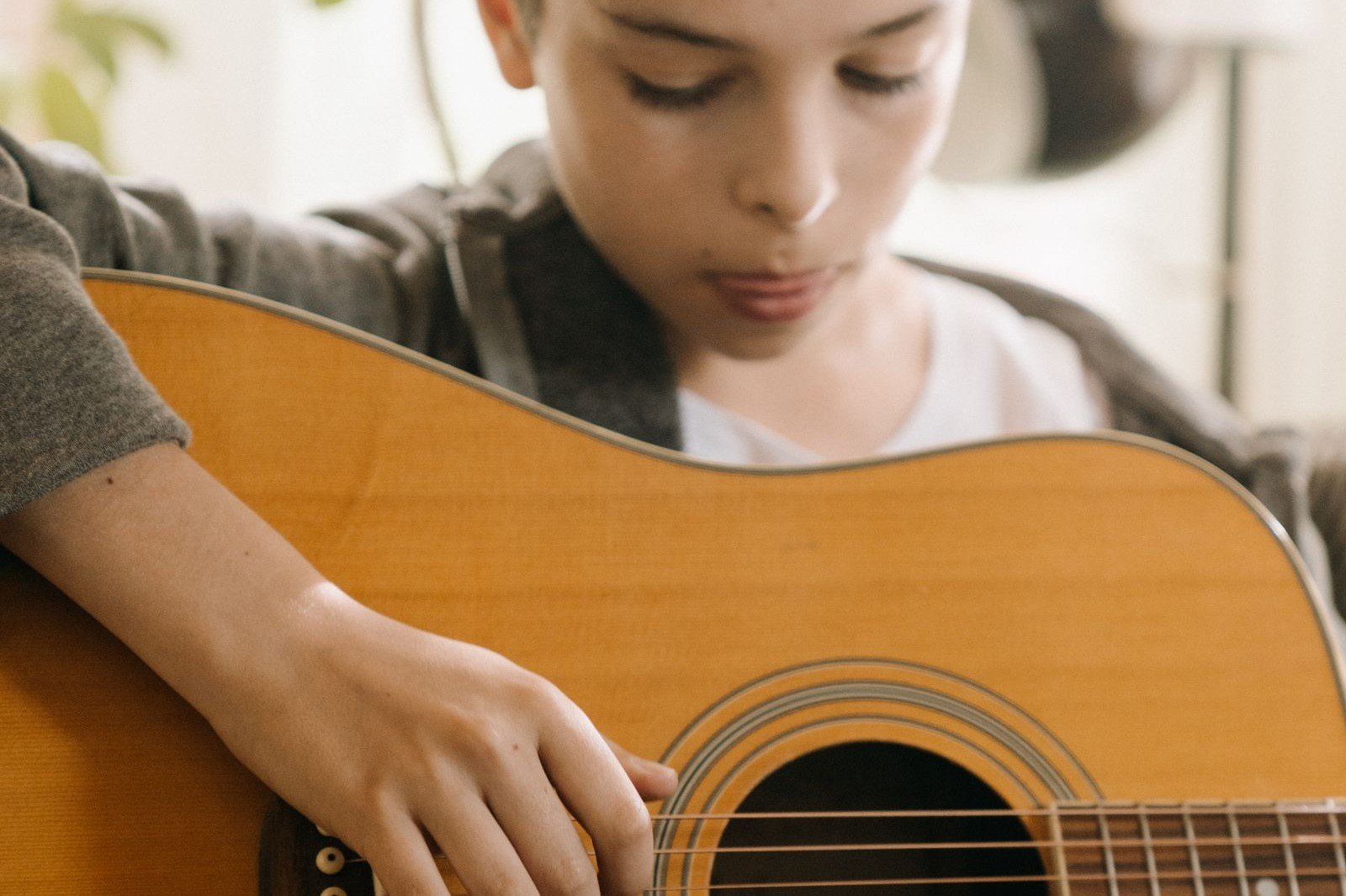 A young beginner focused on picking near the soundhole of an acoustic guitar
