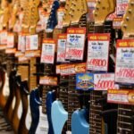 A row of guitars on display in a music shop with price tags attached to each headstock