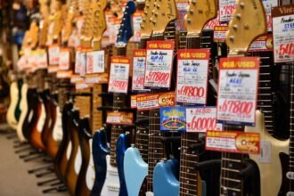 A row of guitars on display in a music shop with price tags attached to each headstock