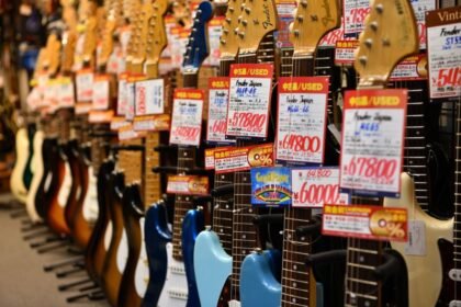A row of guitars on display in a music shop with price tags attached to each headstock