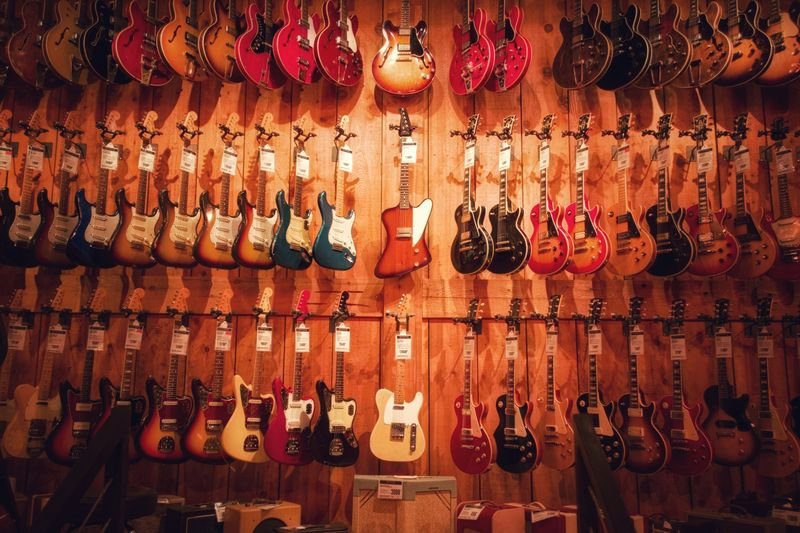 Rows of electric guitars hanging on a wooden shop wall, each with a small price tag attached