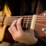 Close-up of a hand fretting a chord on an acoustic guitar neck, showing fret spacing