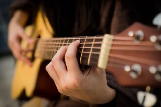 Close-up of a hand fretting a chord on an acoustic guitar neck, showing fret spacing