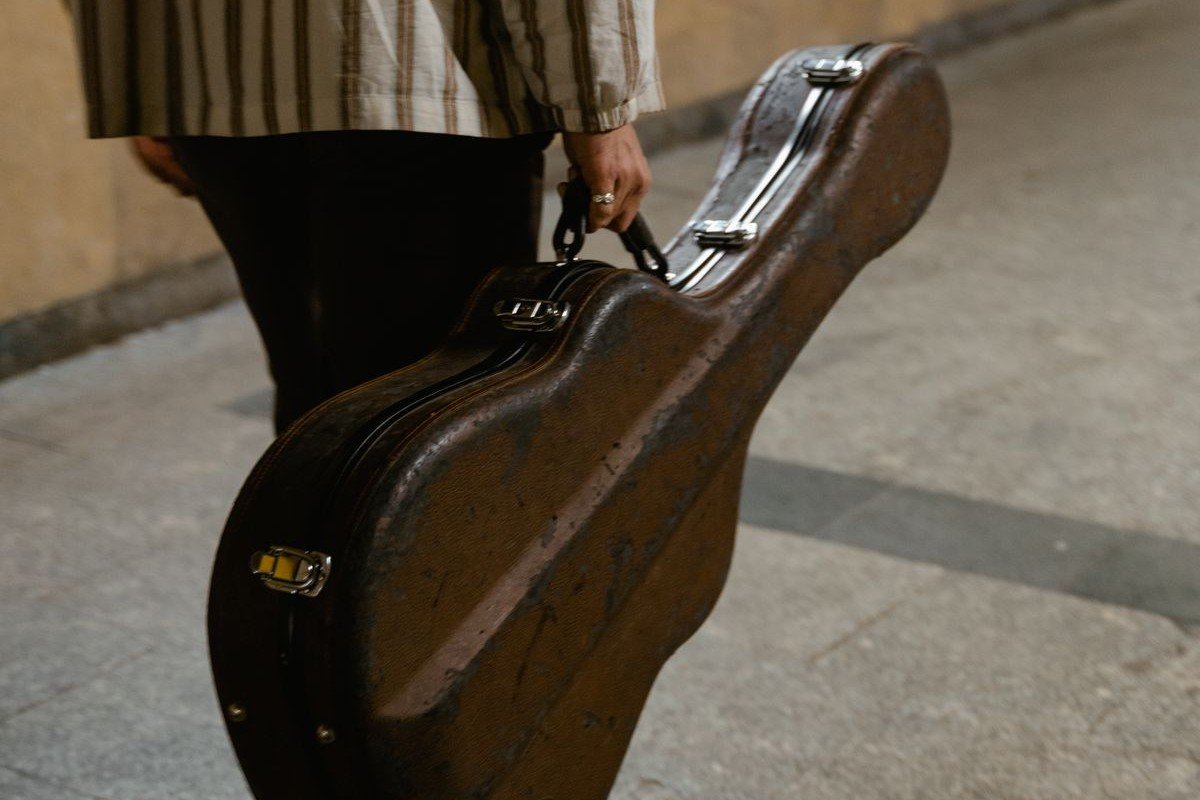 A person carrying a full-size hard guitar case by its handle on a city street