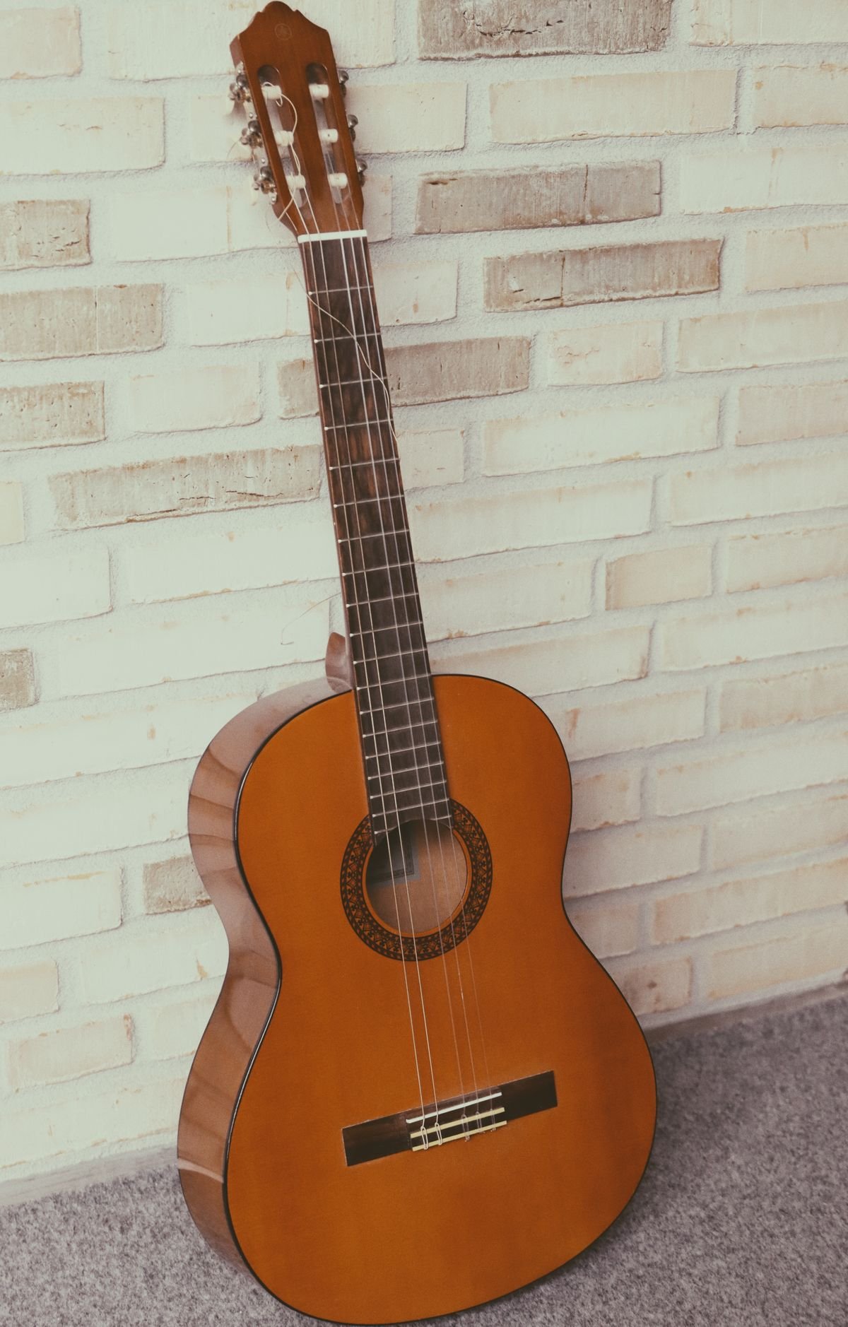 A full-size classical guitar leaning against a brick wall, showing its full length