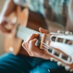 Close-up of a hand fretting a guitar near the nut and headstock