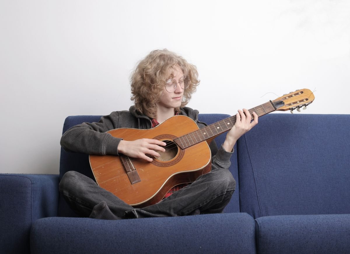A person sitting cross-legged on a sofa playing a compact acoustic guitar