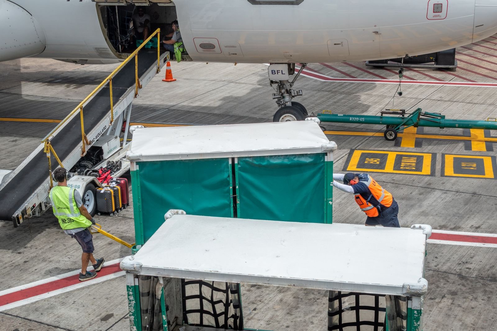 Ground crew loading luggage from a container onto an aircraft hold conveyor