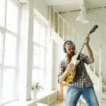 Guitarist playing a solid-body electric guitar through headphones in a bright room, the kind of quiet practice a travel electric guitar is built for