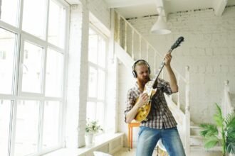 Guitarist playing a solid-body electric guitar through headphones in a bright room, the kind of quiet practice a travel electric guitar is built for