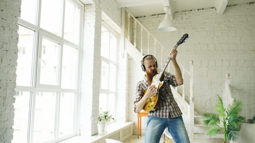 Guitarist playing a solid-body electric guitar through headphones in a bright room, the kind of quiet practice a travel electric guitar is built for