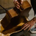 A musician carefully fits an acoustic guitar body into a hardshell case, illustrating the packing problem travel guitars solve
