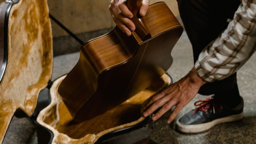 A musician carefully fits an acoustic guitar body into a hardshell case, illustrating the packing problem travel guitars solve