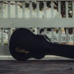 Black hard guitar case standing against a white fence, the kind of case insurers expect an instrument to travel in