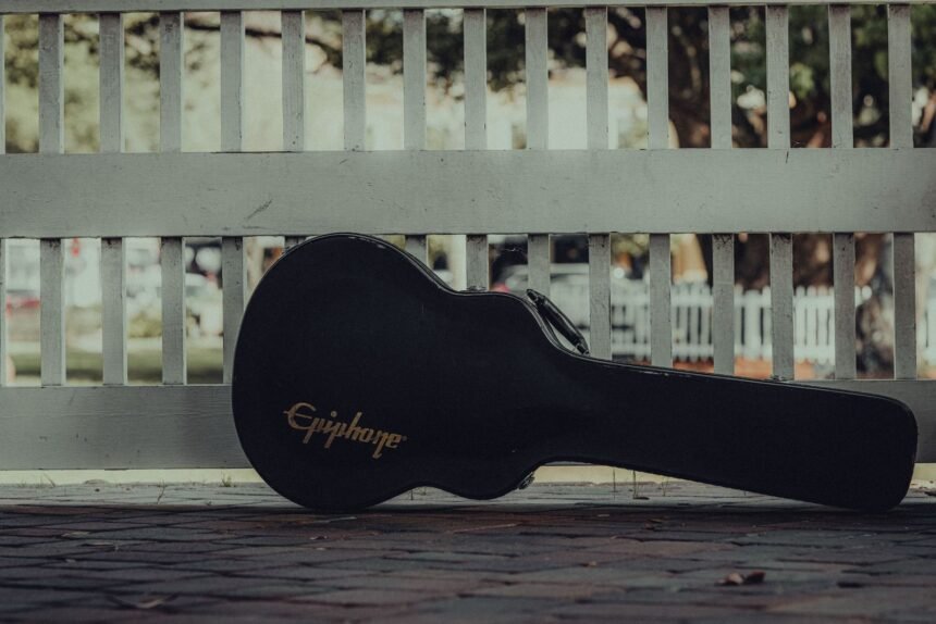 Black hard guitar case standing against a white fence, the kind of case insurers expect an instrument to travel in