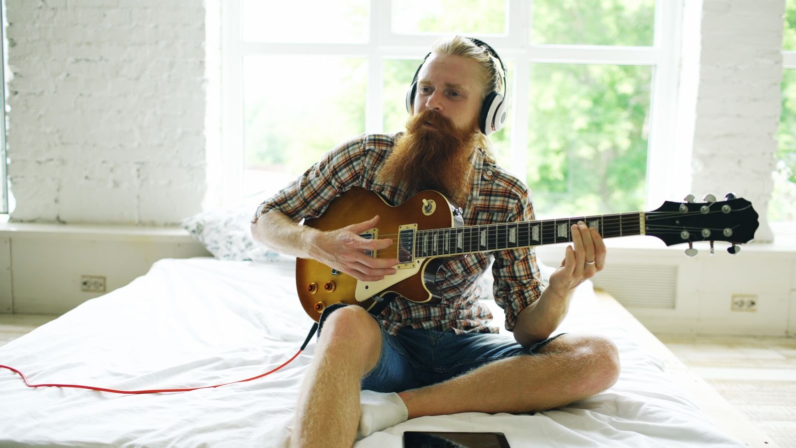 Guitarist sitting cross-legged playing an electric guitar through headphones for silent practice