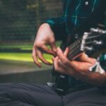 A musician's hands fingerpicking a bass guitar, illustrating the compact ultra-light travel bass format